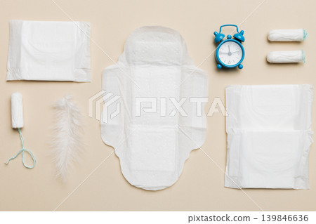 Ringing alarm clock with sanitary female tampons and menstrual sanitary pads. Medical concept of woman critical days and menstruation. Female daily hygiene. Copy space Ringing alarm clock with sanitary female tampons and menstrual sanitary pads. Medical concept of woman critical days and menstruation. Female daily hygiene. Copy space 139846636