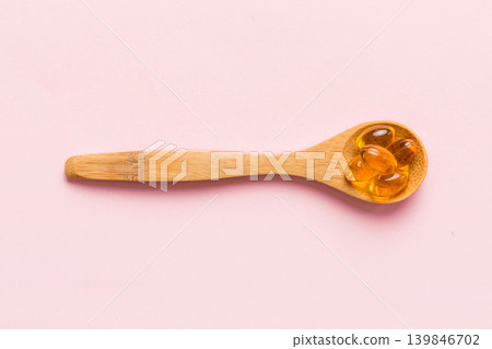 Vitamin omega capsules in a spoon on a colored background. Pills served as a healthy meal. Red soft gel vitamin supplement capsules on spoon 139846702