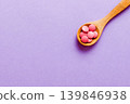 Vitamin capsules in a spoon on a colored background. Pills served as a healthy meal. Red soft gel vitamin supplement capsules on spoon 139846938