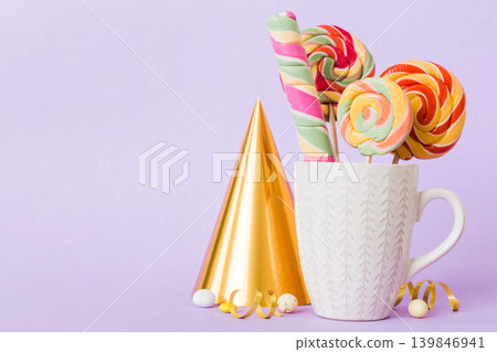 Colorful candies in cup on table on light background background. Large swirled lollipops. Creative concept of a jar full of delicious sweets from the candy store Colorful candies in cup on table on light background background. Large swirled lollipops. Creative concept of a jar full of delicious sweets from the candy store 139846941