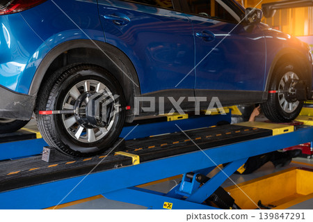 Wheel alignment equipment grip the tire of car wheel in car repair shop. Auto wheel alignment in workshop of service station. Car wheel balance. Suspension adjustment. Vehicle inside garage workshop. 139847291