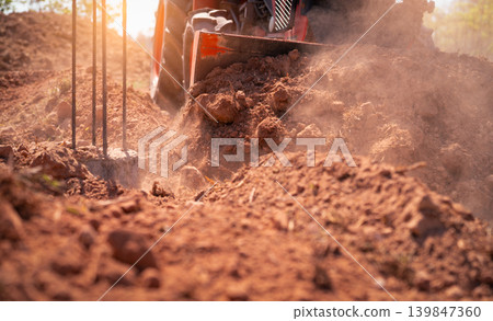 Construction tractor with specialized dozer blade pushing and grading soil at excavation site. Heavy machinery transforming raw land into prepared foundation for upcoming building development project. Construction tractor with specialized dozer blade pushing and grading soil at excavation site. Heavy machinery transforming raw land into prepared foundation for upcoming building development project. 139847360