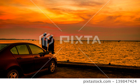 Silhouette of happy couple standing beside car at seaside during dramatic sunset, romantic travel lifestyle concept featuring peaceful coastal atmosphere, love relationship and vacation destination. Silhouette of happy couple standing beside car at seaside during dramatic sunset, romantic travel lifestyle concept featuring peaceful coastal atmosphere, love relationship and vacation destination. 139847424