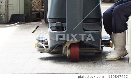 Industrial floor scrubber machine in facility with worker wearing white rubber boots resting after cleaning process. Janitorial service maintenance hygiene and sanitation in workplace environment. Industrial floor scrubber machine in facility with worker wearing white rubber boots resting after cleaning process. Janitorial service maintenance hygiene and sanitation in workplace environment. 139847432
