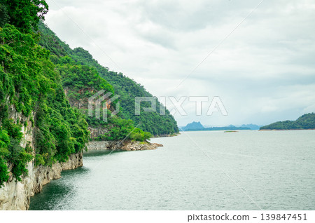 Green mountains and calm dam reservoir water under overcast sky. Sustainable hydroelectric power and environmental conservation. Renewable energy sustainability. Sustainable energy infrastructure. Green mountains and calm dam reservoir water under overcast sky. Sustainable hydroelectric power and environmental conservation. Renewable energy sustainability. Sustainable energy infrastructure. 139847451