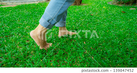 Close-up of barefoot person stepping on lush green grass lawn. Nature connection and natural healing through walking outdoors. Peaceful wellness retreat. Mindful lifestyle and connection to the earth. 139847452