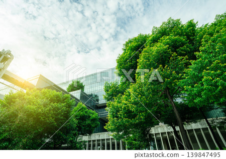 Sustainable green building. Eco-friendly building. Sustainable glass office building with tree for reducing carbon dioxide. Office with green environment. Corporate building reduce CO2. Safety glass. Sustainable green building. Eco-friendly building. Sustainable glass office building with tree for reducing carbon dioxide. Office with green environment. Corporate building reduce CO2. Safety glass. 139847495