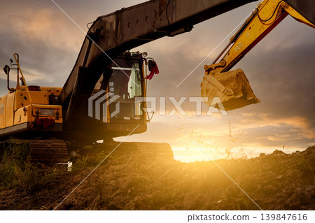 Backhoe at construction site digging soil with bucket of backhoe. Bulldozer on sunset sky. Digger parked at construction site. Earth moving machine. Digger with bucket. Backhoe bucket loading soil. 139847616