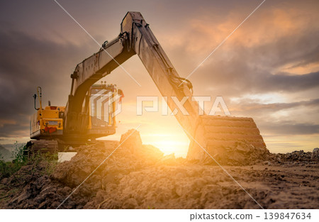Backhoe parked at construction site after digging soil. Bulldozer on sunset sky and clouds background. Digger after work. Earth moving machine at construction site at dusk. Digger with dirt bucket. Backhoe parked at construction site after digging soil. Bulldozer on sunset sky and clouds background. Digger after work. Earth moving machine at construction site at dusk. Digger with dirt bucket. 139847634