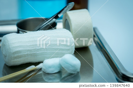 Medical wound dressing equipment on stainless steel tray including antiseptic cotton, surgical tape, forceps and conform bandage, clinical healthcare setup for emergency treatment, nursing care. 139847640