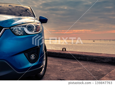 Blue compact SUV car with sport and modern design parked on concrete road by the sea at sunset in the evening. Hybrid and electric car technology concept. Car parking space. Automotive industry. Blue compact SUV car with sport and modern design parked on concrete road by the sea at sunset in the evening. Hybrid and electric car technology concept. Car parking space. Automotive industry. 139847763