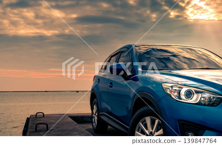 Blue compact SUV car with sport and modern design parked on concrete road by the sea at sunset in the evening. Hybrid and electric car technology concept. Car parking space. Automotive industry. Blue compact SUV car with sport and modern design parked on concrete road by the sea at sunset in the evening. Hybrid and electric car technology concept. Car parking space. Automotive industry. 139847764