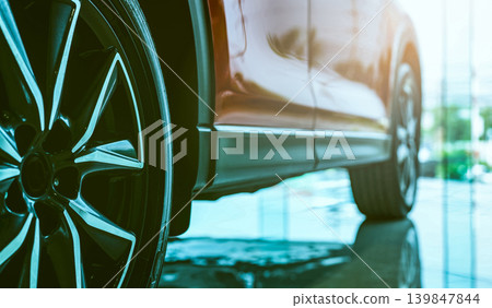 Luxury car parked in modern showroom. Auto leasing business. Car dealership concept. Closeup wheel of red shiny car show in showroom. Automotive industry. Auto glass coating and shinning business. Luxury car parked in modern showroom. Auto leasing business. Car dealership concept. Closeup wheel of red shiny car show in showroom. Automotive industry. Auto glass coating and shinning business. 139847844