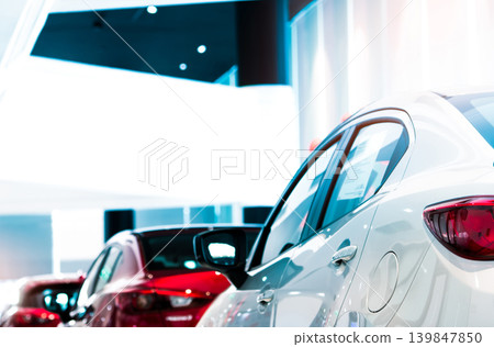 Rear view of white luxury car parked in modern showroom for sale. White shiny car on blurred red car in showroom. Car dealership. Coronavirus impact on automotive industry concept. Showroom interior. Rear view of white luxury car parked in modern showroom for sale. White shiny car on blurred red car in showroom. Car dealership. Coronavirus impact on automotive industry concept. Showroom interior. 139847850
