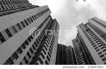 Bottom view of skyscraper building looking up against gray sky. Urban apartment, multi storey residential condo, corporate construction, and real estate development in city environment. Bottom view of skyscraper building looking up against gray sky. Urban apartment, multi storey residential condo, corporate construction, and real estate development in city environment. 139847902