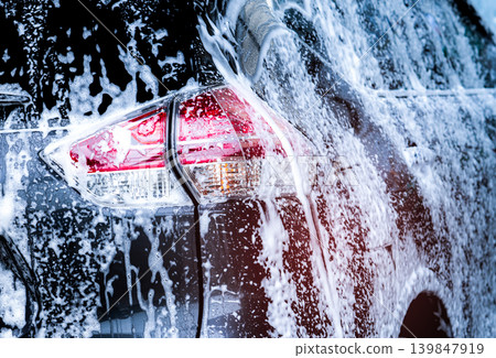 Rear view of black compact SUV car with sport and modern design are washing with water and white foam. Car care service business. Car covered with white foam. Car wash before and after travel concept. Rear view of black compact SUV car with sport and modern design are washing with water and white foam. Car care service business. Car covered with white foam. Car wash before and after travel concept. 139847919