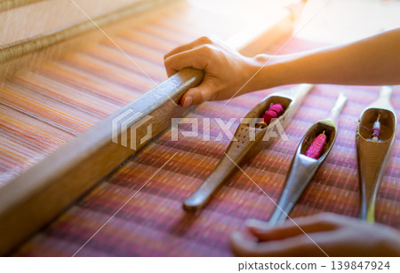 Woman working on weaving machine for weave handmade fabric. Textile weaving. Weaving using traditional hand weaving loom on cotton strands. Textile or cloth production in Thailand. Asian culture. Woman working on weaving machine for weave handmade fabric. Textile weaving. Weaving using traditional hand weaving loom on cotton strands. Textile or cloth production in Thailand. Asian culture. 139847924