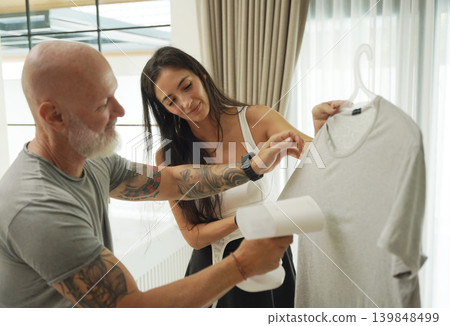A couple ironing a t-shirt with a steam iron. A couple ironing a t-shirt with a steam iron. 139848499