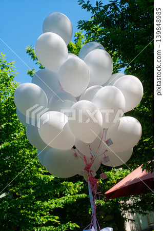 Cluster of White Balloons Floating Outdoors Over Green Trees and Bright Blue Sky Cluster of White Balloons Floating Outdoors Over Green Trees and Bright Blue Sky 139848985