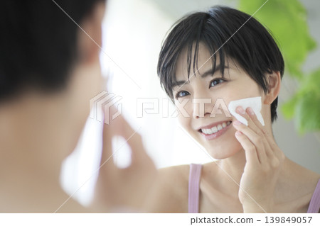 一位女士正在對著鏡子進行護膚,用化妝棉擦拭皮膚,為美容做好準備。 一位女士正在對著鏡子進行護膚,用化妝棉擦拭皮膚,為美容做好準備。 139849057