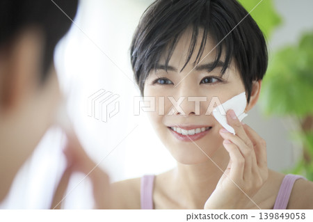 A smiling woman applying skincare products with cotton pads: Morning beauty routine, beauty image. A smiling woman applying skincare products with cotton pads: Morning beauty routine, beauty image. 139849058