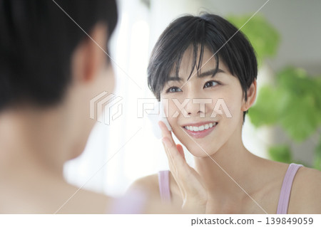 一位女性在鏡子前進行護膚:美麗與自我關懷的象徵。 一位女性在鏡子前進行護膚:美麗與自我關懷的象徵。 139849059