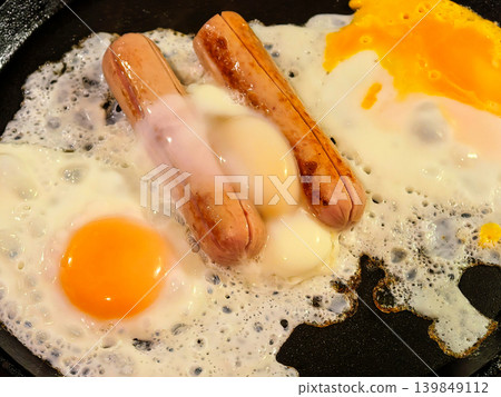 Fried eggs and sausages cooking in pan Fried eggs and sausages cooking in pan 139849112