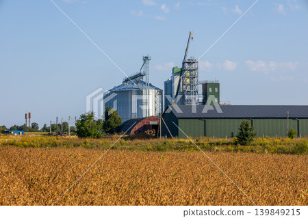 Agricultural field shows grain silos and a storage building in a farmland setting under clear skies Agricultural field shows grain silos and a storage building in a farmland setting under clear skies 139849215
