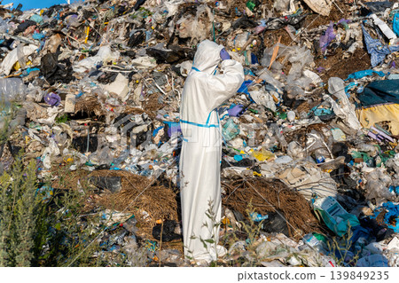Environmentalist in white protective suit stands at a landfill site to study the effects of waste on the ecosystem and explore solutions Environmentalist in white protective suit stands at a landfill site to study the effects of waste on the ecosystem and explore solutions 139849235