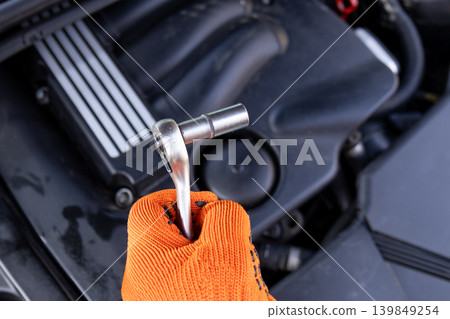 A mechanic holds a ratchet tool while working on a car engine in a garage. The scene shows hands in orange gloves focused on the task A mechanic holds a ratchet tool while working on a car engine in a garage. The scene shows hands in orange gloves focused on the task 139849254