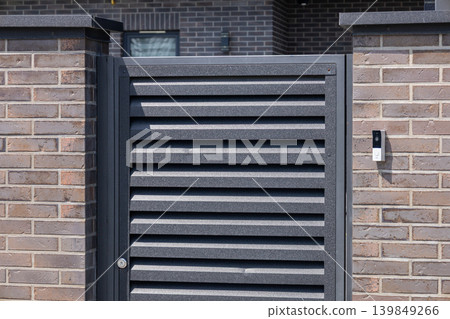 Modern gate stands at the entrance with intercom system installed on the wall. It provides access to a private residence Modern gate stands at the entrance with intercom system installed on the wall. It provides access to a private residence 139849266