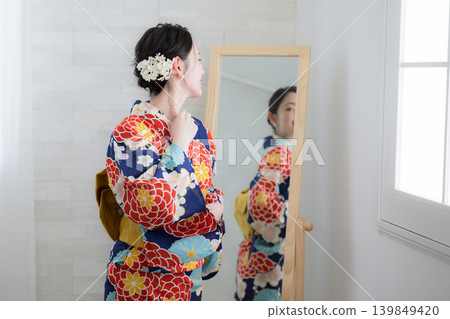 一位日本女性準備穿浴衣，對著鏡子檢查自己的裝扮（未露出臉部）。 139849420