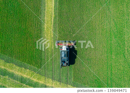 Top down view shows a large combine harvester cuts rows of green crops in a sprawling farm field under a bright blue sky Top down view shows a large combine harvester cuts rows of green crops in a sprawling farm field under a bright blue sky 139849471