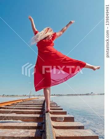 A woman with colorful dreadlocks walks barefoot on rusted railway tracks at Bursol salt lake, Russia A woman with colorful dreadlocks walks barefoot on rusted railway tracks at Bursol salt lake, Russia 139849491
