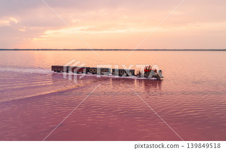 Aerial view captures specialized locomotive pulls several wagons across the strikingly pink waters of Bursol Lake Aerial view captures specialized locomotive pulls several wagons across the strikingly pink waters of Bursol Lake 139849518