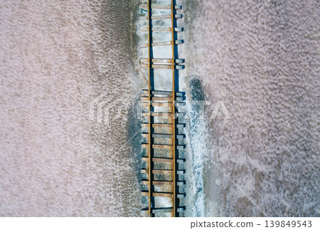 Rusty railway tracks with wooden sleepers run across a textured pink and white salt flat. Lake Bursol, Russia Rusty railway tracks with wooden sleepers run across a textured pink and white salt flat. Lake Bursol, Russia 139849543