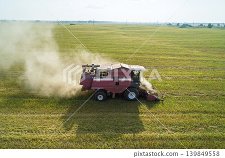 A powerful combine harvester cuts and processes crops in a wide green field, creating a large dust cloud. A powerful combine harvester cuts and processes crops in a wide green field, creating a large dust cloud. 139849558