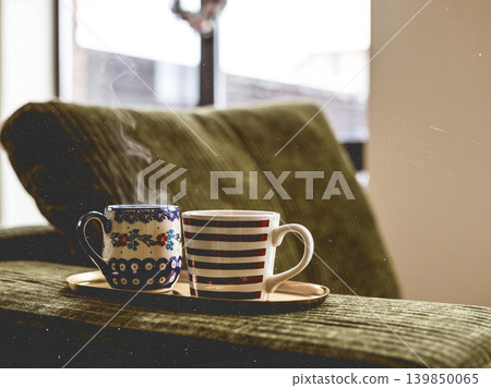 Cozy home winter vibes. Two mugs with hot drinks on a tray on a green corduroy sofa, warmth, relaxation indoors. Hot tea in mugs Cozy home winter vibes. Two mugs with hot drinks on a tray on a green corduroy sofa, warmth, relaxation indoors. Hot tea in mugs 139850065