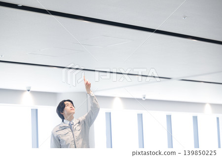 一名年輕的技術員正在對樓宇設備進行維護工作,他指著天花板。 一名年輕的技術員正在對樓宇設備進行維護工作,他指著天花板。 139850225