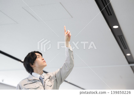 一名年輕的技術員正在對樓宇設備進行維護工作，他指著天花板。 139850226