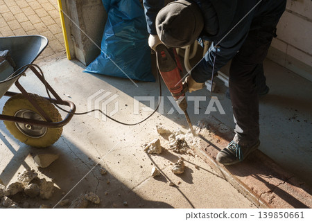 Worker using jackhammer to break concrete floor during renovation 139850661