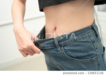 Young Asian woman losing weight wearing loose pants in oversize jeans. 139851136