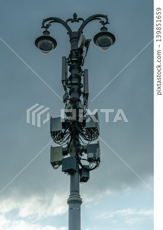 Urban Street Lamp Pole With Mounted Cellular Antennas and Telecom Equipment Against Cloudy Sky Urban Street Lamp Pole With Mounted Cellular Antennas and Telecom Equipment Against Cloudy Sky 139851659