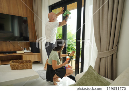 A man and woman wash windows in their home together 139851770