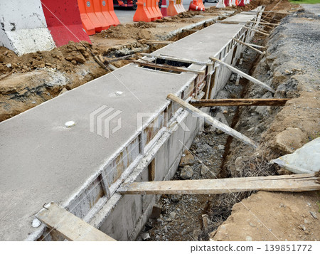 Narrow ditch with reinforcement, waterproof concrete trench bounded by soil and support stakes Narrow ditch with reinforcement, waterproof concrete trench bounded by soil and support stakes 139851772