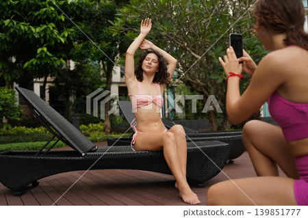 A woman captures her friend's relaxed pose while sitting on a lounge chair A woman captures her friend's relaxed pose while sitting on a lounge chair 139851777