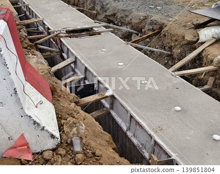 Narrow ditch with reinforcement, waterproof concrete trench bounded by soil and support stakes 139851804