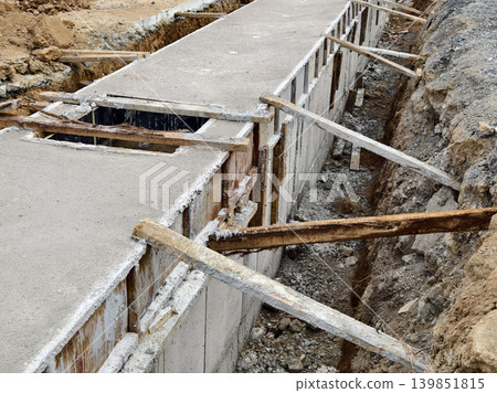 Narrow ditch with reinforcement, waterproof concrete trench bounded by soil and support stakes Narrow ditch with reinforcement, waterproof concrete trench bounded by soil and support stakes 139851815