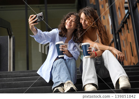 Two young women drink coffee and take pictures near the entrance to the office. Two young women drink coffee and take pictures near the entrance to the office. 139851842