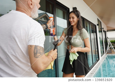 A man and woman wash windows in their home together A man and woman wash windows in their home together 139851920